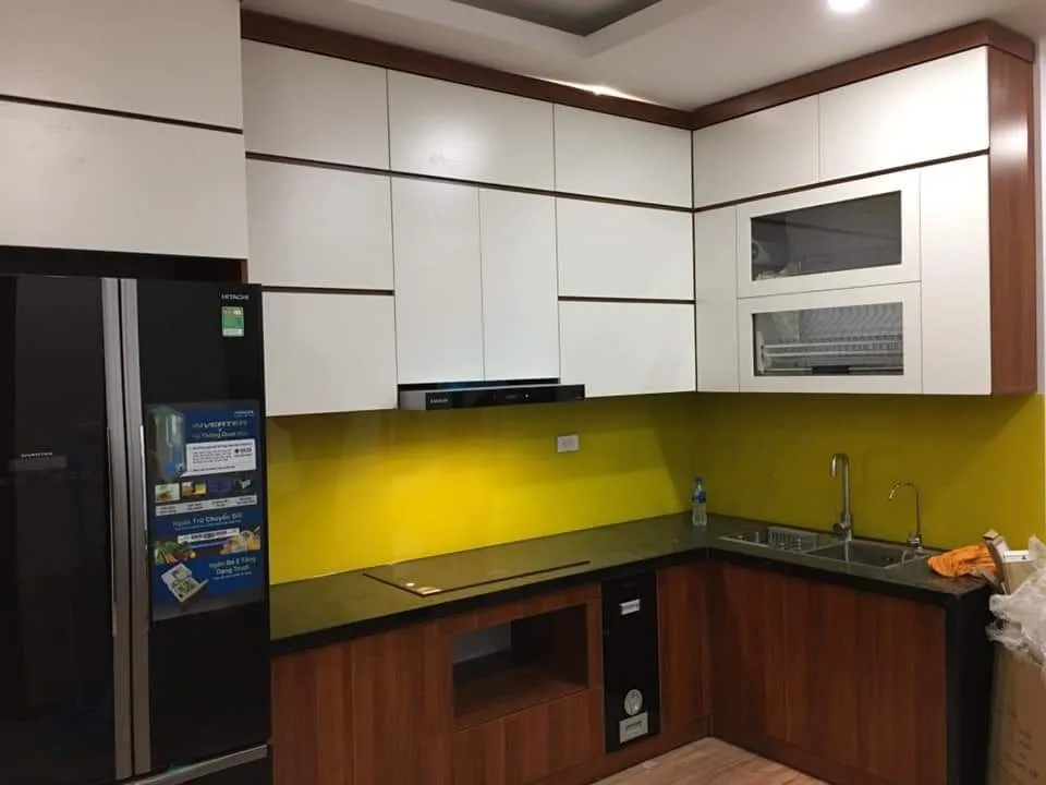 Tủ bếp chữ L cánh vân gỗ đỏ nâu phối tủ trên trắng và kính ốp vàng