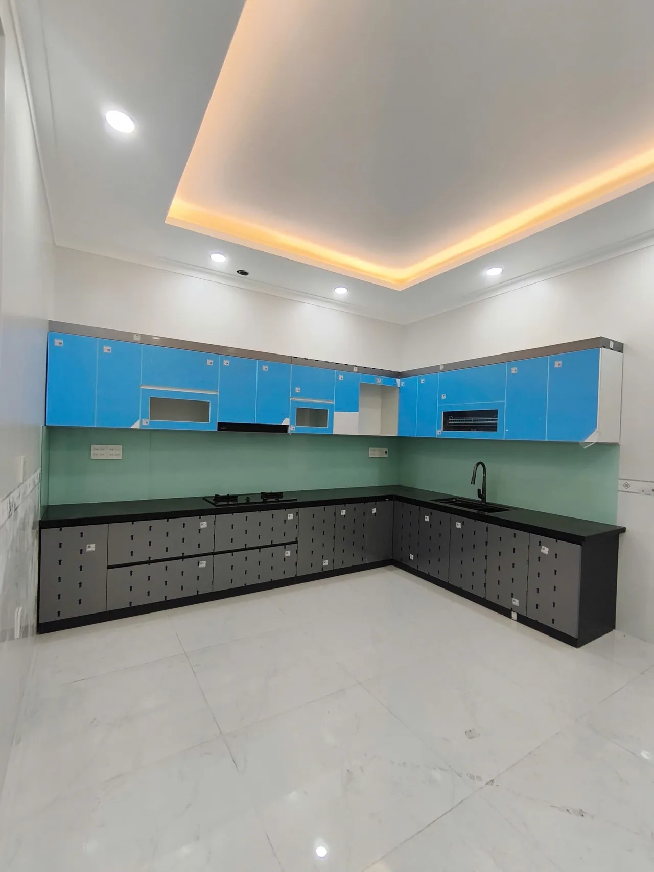 Bếp chữ L với cánh còn tem, mặt bàn tối và khoảng tường phía trên tủ treo