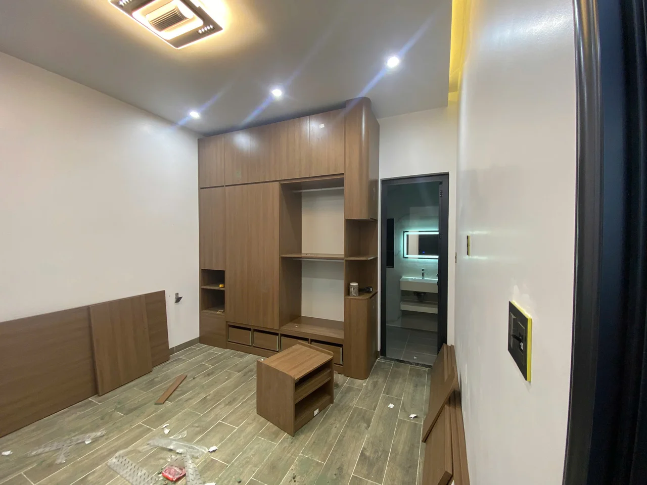 Góc phòng có tủ tông gỗ, cấu kiện giường đặt trên sàn và mảng tường trơn