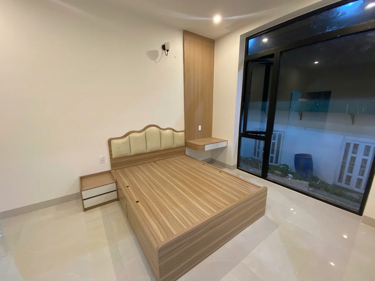 Giường tông gỗ với đầu giường bọc sáng màu, hai tab và cửa sổ lớn khung tối