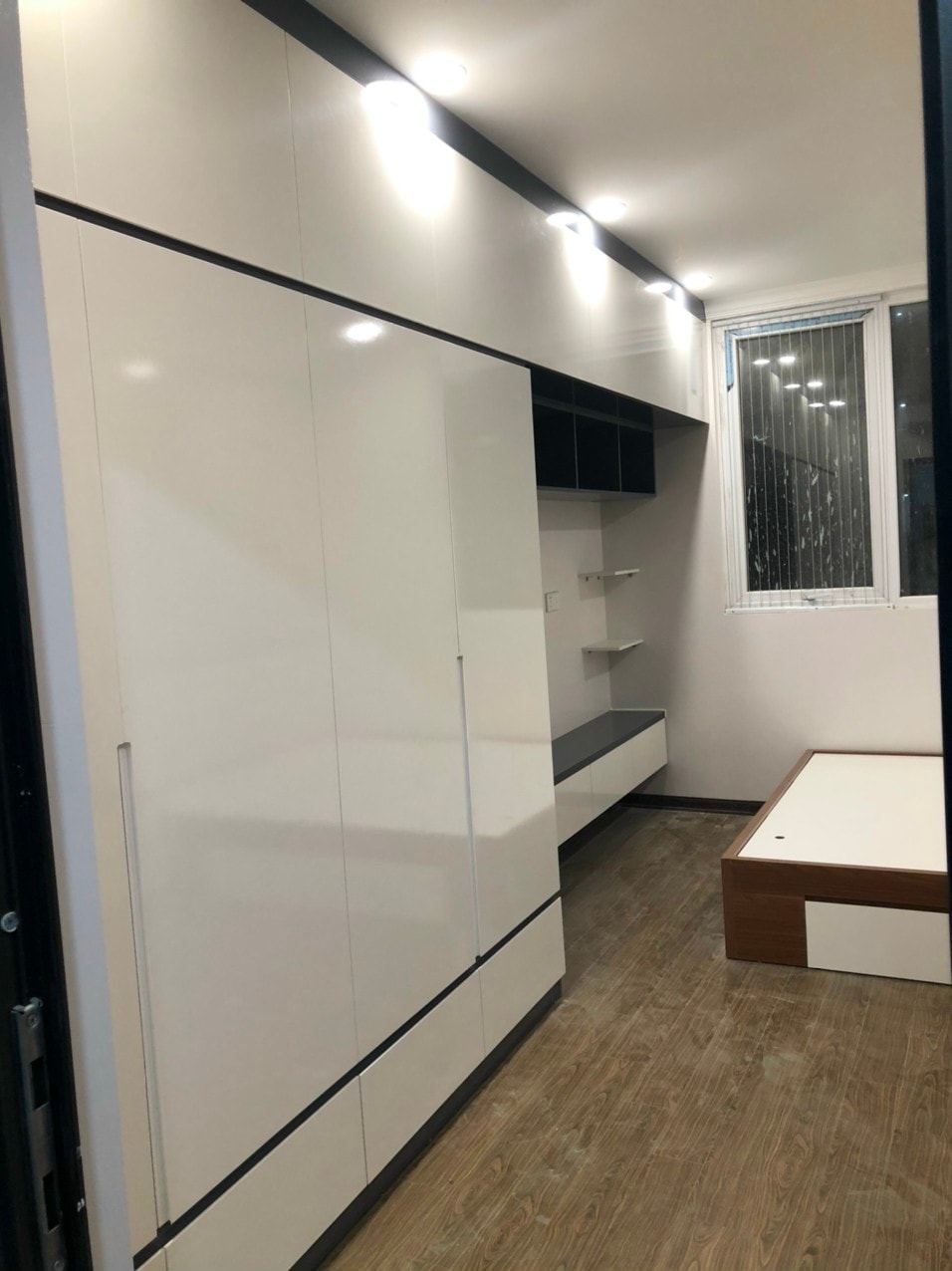 Phòng ngủ gỗ MDF với mảng vách nan sọc dọc, giường ngủ tựa nệm nỉ và gương tròn treo